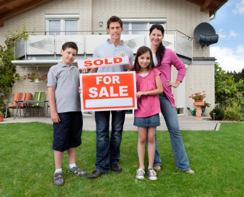 Portrait of happy young family in front of new home with sold real estate sign